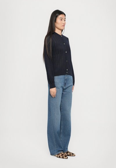 Tumši zilā adīta pogājama džemperis ar garām piedurknēm un struktūras rakstu. Kombinēts ar gaiši ziliem platām biksēm un leoparda raksta apaviem.