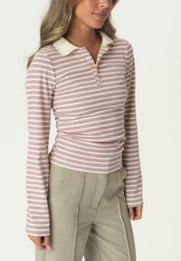 Langärmeliges Poloshirt mit hellrosa und cremefarbenen horizontalen Streifen, ausgestattet mit einem cremefarbenen Kragen und einer Knopfleiste, kombiniert mit hellgrauen Hosen.