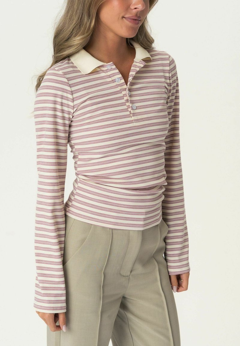 Langärmeliges Poloshirt mit hellrosa und cremefarbenen horizontalen Streifen, ausgestattet mit einem cremefarbenen Kragen und einer Knopfleiste, kombiniert mit hellgrauen Hosen.