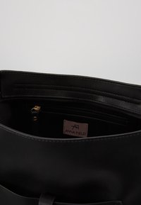 Wnętrze czarnej skórzanej torby z kieszenią na zamek, wewnątrz której znajduje się brązowa metka z logo marki Anna Field.