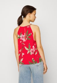 Top sem mangas floral vermelho com costas altas, apresentando padrões de flores em rosa e verde, e um detalhe em forma de buraco na gola.