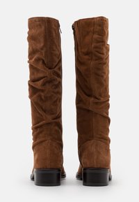 Bottes hauteur genou en daim marron avec un design plissé, dotées d'une fermeture éclair latérale et d'un bout légèrement arrondi. Talon noir robuste.