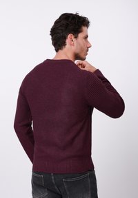 Pull en tricot bordeaux avec des accents de manches côtelées et un corps texturé. Col rond, taille ajustée et style décontracté.
