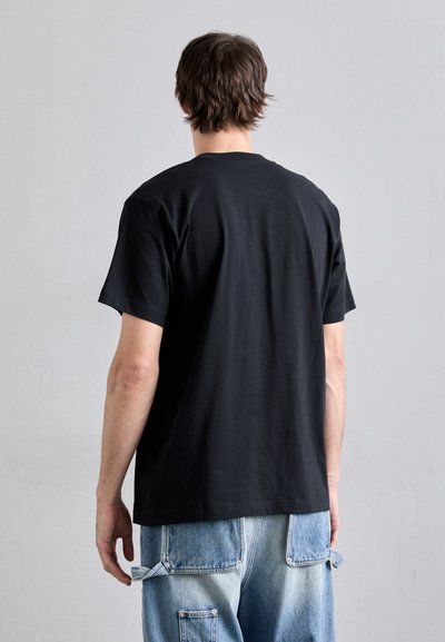 T-shirt en coton noir à manches courtes, col rond et design épuré, associé à un jean cargo bleu clair avec de multiples poches.