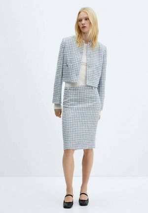 Costume en tweed bleu et blanc avec une veste courte et une jupe crayon. Présente un motif texturé et des accents en métal argenté. Chaussures noires.