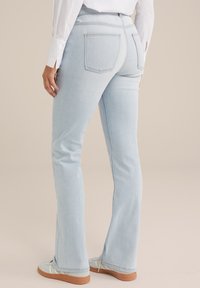Vaqueros de mezclilla de color azul claro con pata de elefante y una textura suave, que cuentan con dos bolsillos traseros y una cintura de altura media, combinados con zapatillas ligeras.