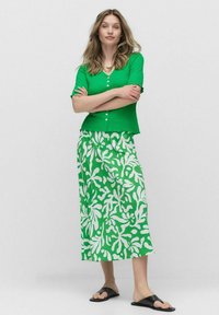Grön texturerad kortärmad topp med knappar, tillsammans med en lång grön kjol med ett vitt blommönster. Svarta slidesandaler.