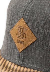 Căciulă gri din material texturat, cu un patch cu diamante din piele ecologică maro, având logo și cusături, și un vizor cu carouri maro și negru.