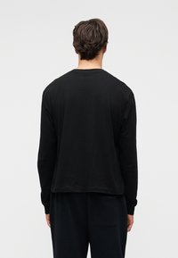 Μαύρο βαμβακερό μακρυμάνικο t-shirt με άνετη εφαρμογή, στρογγυλή λαιμόκοψη και μινιμαλιστικό σχέδιο, εμφανιζόμενο από πίσω.