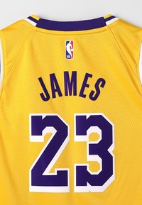 Žlutý basketbalový dres s fialovými a bílými detaily, zobrazuje "JAMES" a číslo "23" ve fialové barvě, s logem NBA nahoře.