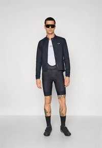 Meeste spordiriietus, mis koosneb tumelainest lukuga jopest, valgest vormis särgist, mustadest jalgrattapükstest, pikkadest sokkidest ja päikeseprillidest. Siledad tekstuurid ja sportlik disain.