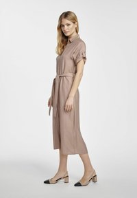 Koszula sukienka w kolorze zapylonego różu z krótkimi, zrolowanymi rękawami, zapinana na guziki z przodu i z paskiem w talii. Połączona z dwutonowymi sandałami na słupku.
