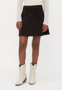 Jupe en velours côtelé marron avec un ourlet évasé, associée à des bottes de cowboy blanches ornées de broderies décoratives et d'un talon bas.