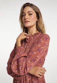 Rochie cu mânecă lungă, de culoare mov, cu un decolteu volănaș și manșete elastice, având modele de flori mici în alb și mov. Textură de țesătură moale.