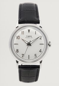 Relógio Timex Marlin com mostrador prateado, pulseira de couro preto, caixa em aço inoxidável, marcadores em algarismos arábicos e movimento de três ponteiros.