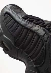 Sort sneaker med en tekstureret læder- og tekstiloverdel, buede paneler og polstret krave, detaljeret med et strømlinet design.