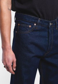 Dark blue denim jeans with orange stitching, a button closure, and front pockets. The fabric has a slight texture and a smooth finish.