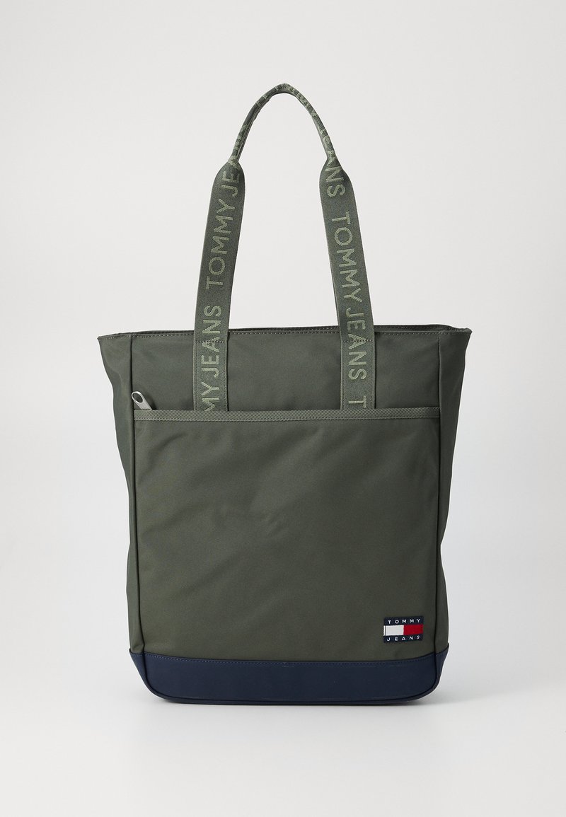 Olivgröna tote-väskor med kontrasterande marinblå botten, dubbla handtag med texten "TOMMY JEANS" och en framficka med dragkedja. Hållbart tyg.