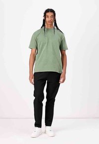 Grünes Baumwoll-T-Shirt mit Rundhalsausschnitt, kombiniert mit schwarzen Hosen und weißen Sneakern. Das T-Shirt hat eine lässige Passform und kurze Ärmel.
