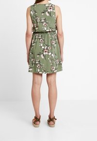 Vestido verde sin mangas con un patrón floral, cintura ceñida y una falda fluida. Combinado con sandalias de cuña marrones.