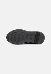 Black rubber sneaker sole with textured grip pattern and embossed brand name. Flat, rounded shape with reinforced edges for durability.