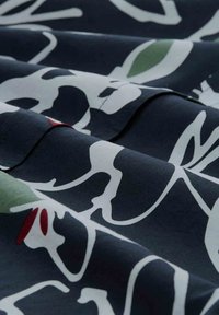 Cotton fabric featuring a dark navy background with large, abstract white and green floral patterns, and small red accents. Smooth texture.