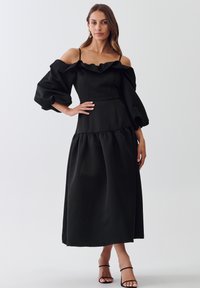 Mustaline must off-shoulder kleit, mis on valmistatud siledast kangast, puffi varrukate, rüüstatud kaeluse ja kihilise hemline'iga.