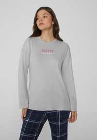 Camisa de manga larga gris con la palabra "SLEEPY" en texto rojo, combinada con pantalones de pijama de cuadros marinos con acentos en azul y rosa.