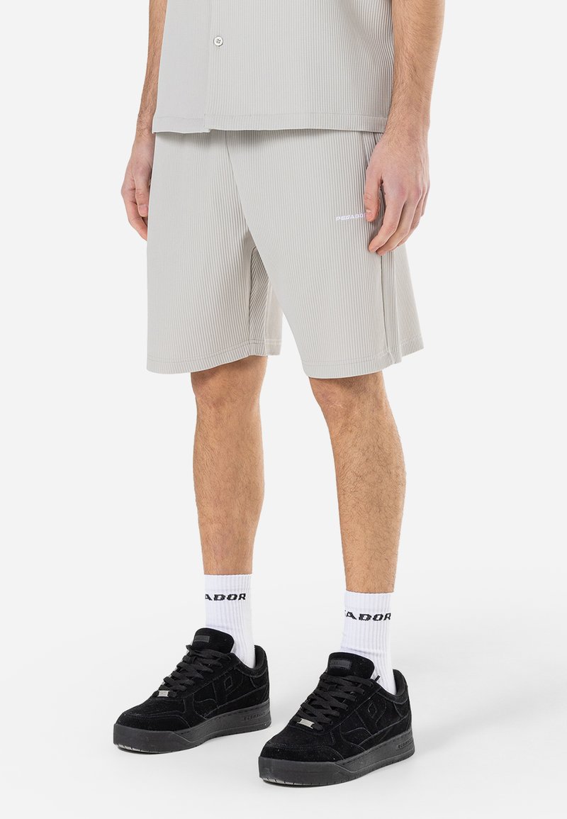 Light grey, ribbed short-sleeve shirt paired with matching shorts. Black suede sneakers with white socks featuring text near the top.