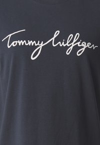 Navy blue t-shirt made of cotton with a rounded neckline. Features a large white script logo "Tommy Hilfiger" across the chest.