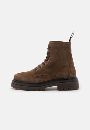 Brown suede ankle boot with round toe, lace-up design, padded collar, and sturdy rubber sole featuring a slight heel and textured accents.