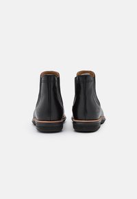 Bottes courtes en cuir noir à finition lisse, doublure beige, semelle en caoutchouc noire solide, avec des détails de coutures minimalistes à l'arrière.