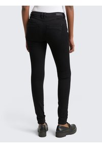 Czarne obcisłe jeansy o gładkiej fakturze, z talią średniego wzrostu, tylnymi kieszeniami oraz przeszyciami. Noszone z czarnymi butami.