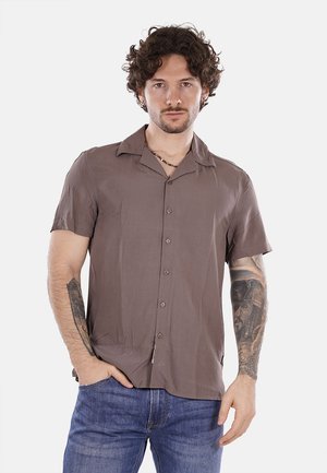 Camicia a maniche corte, marrone chiaro, con colletto ampio, tessuto liscio e taschino sul petto, abbinata a jeans in denim blu.