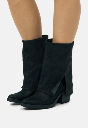 Stivaletti neri in suede con un design morbido, punta affusolata e tacco a blocco. Notevoli dettagli con fessure laterali aumentano l'interesse visivo.