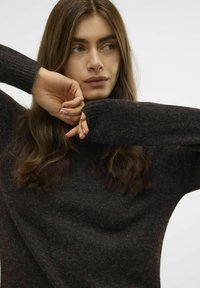 Maglione scuro e testurizzato con una vestibilità ampia e polsini a coste, dotato di un collo rotondo. Il tessuto presenta sottili variazioni di colore.