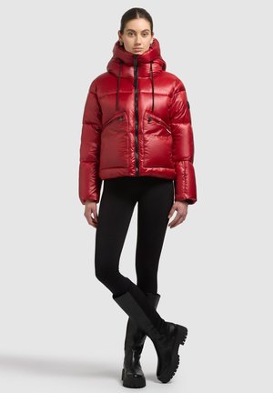 Rode gewatteerde jas met een hoge kraag, ritssluitingen op de zakken en zwarte trekkoordjes. Draagt dit met zwarte legging en zwarte laarzen tot aan de knie.