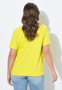 Chemise à rayures jaunes avec des manches courtes et un ourlet arrondi. Le tissu a une texture lisse et présente de légères volants bouffants aux manches.