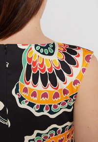 Mekko ilman hihoja, jossa on eläväinen kukkakuosi punaisena, oranssina, vihreänä ja valkoisena mustalla taustalla, takana piilotettu vetoketju.