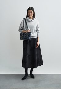 Ανοιχτό γκρι πουλόβερ με λαιμόκοψη, μαύρη φούστα με λουλουδάτα σχέδια από χάντρες, μαύρες γόβες και μια δομημένη ναυτική τσάντα με ζώνη.