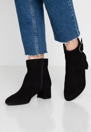 Sorte ankelstøvler i ruskind med blokhæl, udstyret med lynlås i siden og en opbukket manchet. Kombineret med kortere blå denimbukser med flagrende kanter.