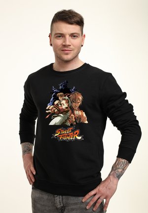 Schwarzer Pullover mit einem Grafikdruck von drei Charakteren aus der "Street Fighter"-Reihe; glattes Material, runder Halsausschnitt, lange Ärmel.