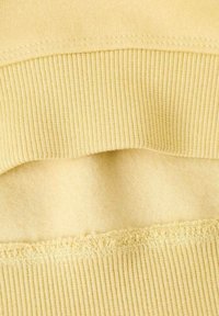 Close-up van gele stof die de ribgebreide textuur en zachte fleece voering laat zien aan de zoom of manchetten van een kledingstuk.
