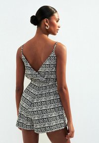 Rompers à motif noir et blanc avec un design à dos en V, fines bretelles et taille élastique, mettant en avant des formes géométriques et des lignes.