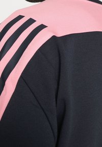 Black athletic shirt with pink shoulder panels featuring three black stripes, showcasing modern sportswear design.