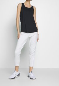 Czarny bezrękawnik i jasnoszare spodnie dresowe. Tank top ma luźny krój; spodnie dresowe są zwężane z bocznymi panelami. Buty są białe z wzorzystymi podeszwami.