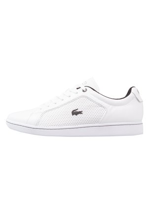 White low-top sneaker with perforated side panel, black crocodile logo, white laces, and black inner lining.