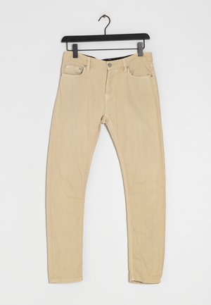 Vaqueros beige de algodón elástico con un corte slim, cinco bolsillos y herrajes metálicos. La tela tiene una textura suave y un color neutro.