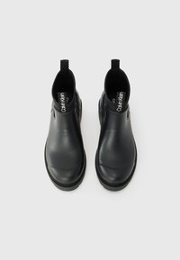 Black, glossy ankle boots with a round toe, elastic sides, and pull tabs on the back. Smooth texture with a rubber sole and subtle branding.