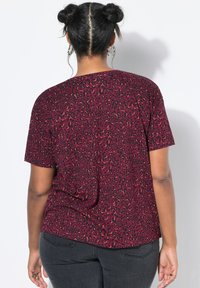 Top rosso a maniche corte con un motivo a stampa leopardata nera e arancione. Tessuto morbido che si drappeggia in modo morbido, con un orlo arrotondato e senza elementi metallici visibili.